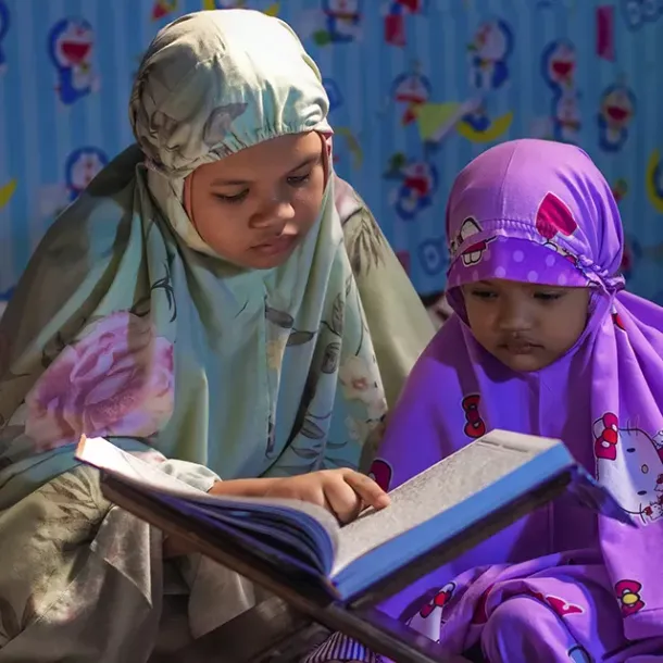 Kakak dan adik belajar membaca Al-Qur'an bersama di rumah
